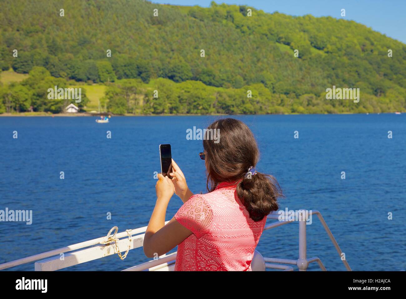 Indian woman tourist enjoying a cruise and taking photographs with her smart phone aboard Ullswater Steamers. Ullswater, UK. Stock Photo