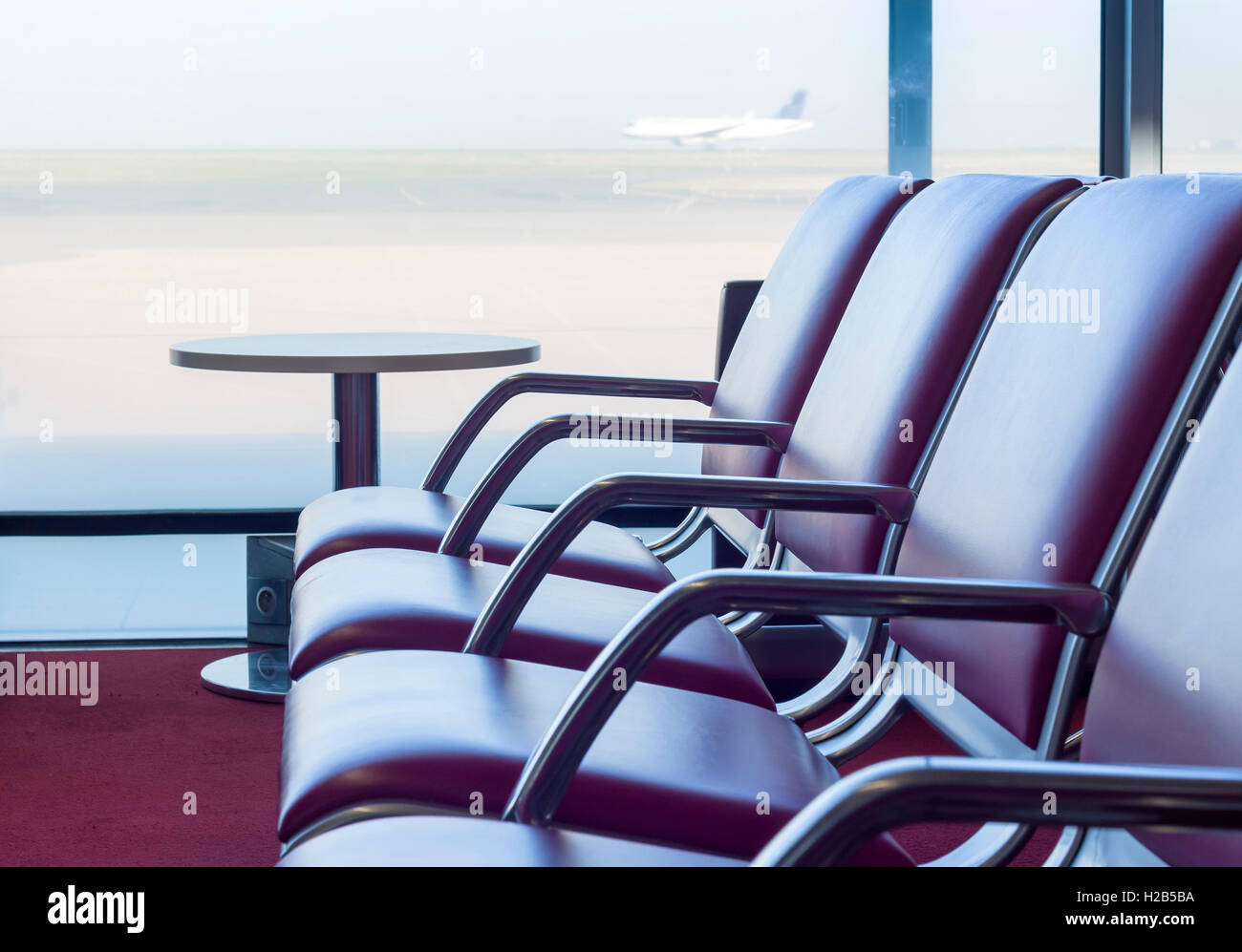 Bench in departure flights waiting hall at the airport with airplane in the background Stock Photo