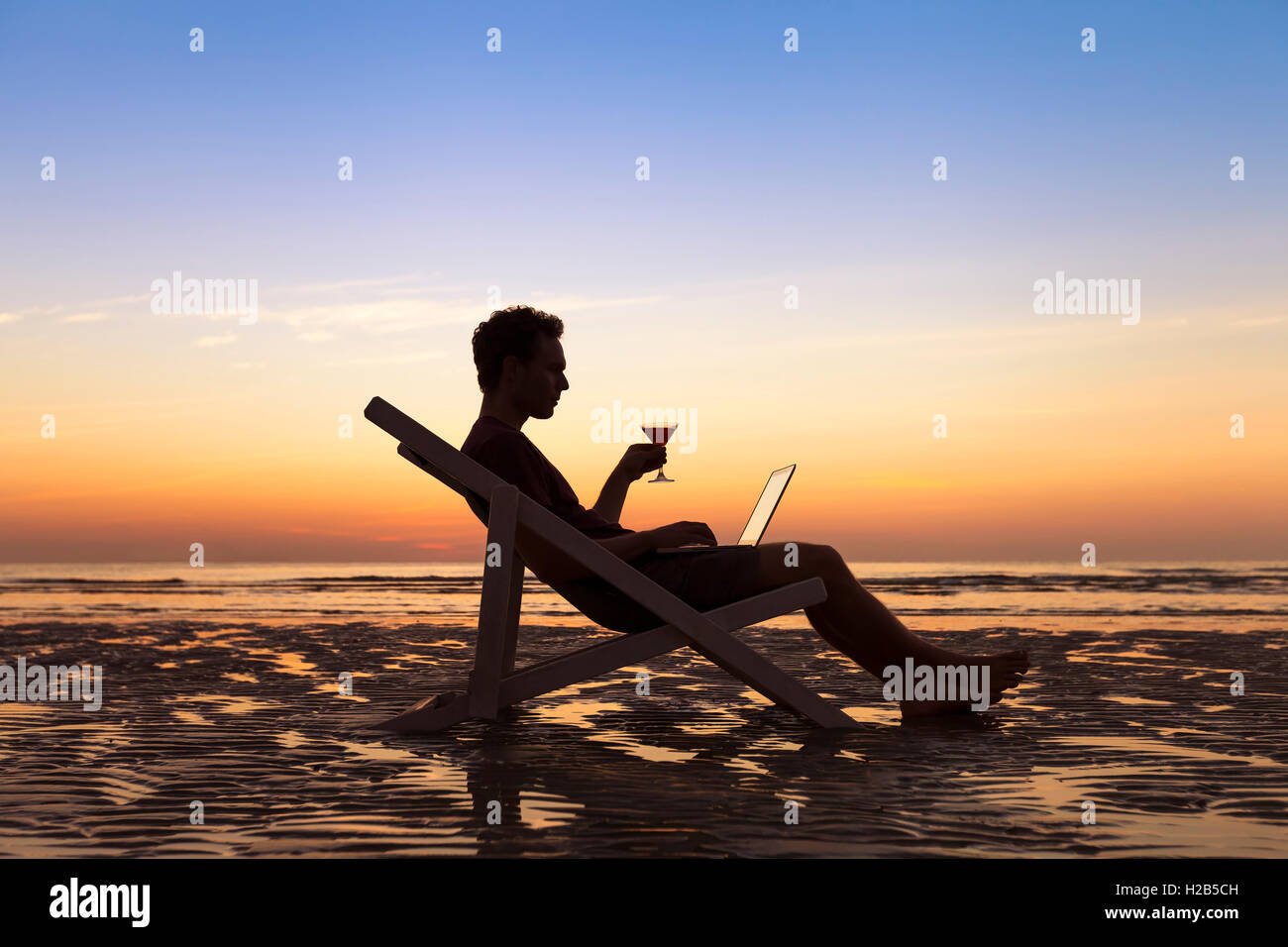 Freelancer sending emails with laptop on tropical beach while traveling Stock Photo