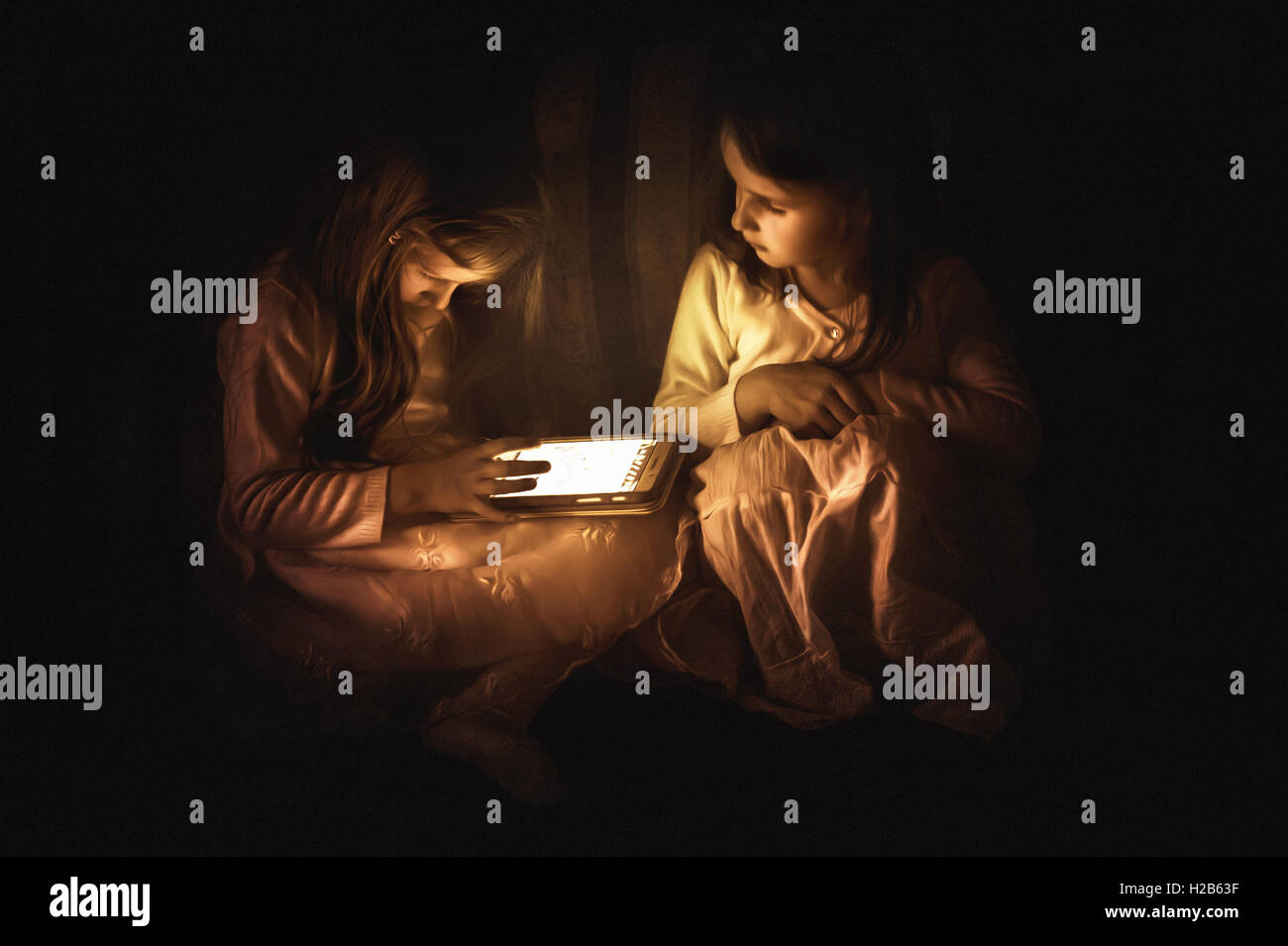 two small girls siting on the coach and looking at the lit tablet Stock Photo