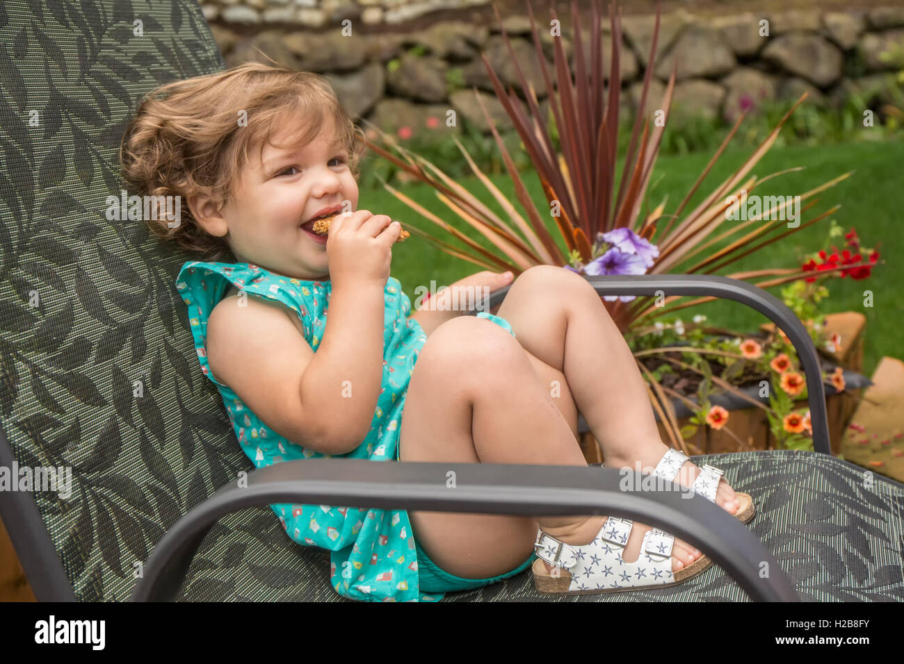 Eighteen month old girl eating a granola bar outside with her mother beside her, in Issaquah, Washington, USA Stock Photo