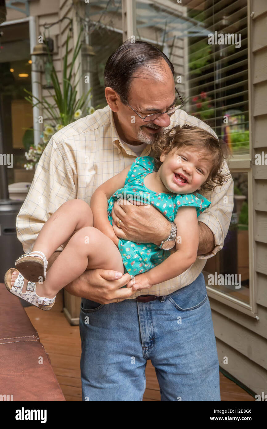 Grandfather playfully holding his fourteen month old granddaughter outside his home Stock Photo