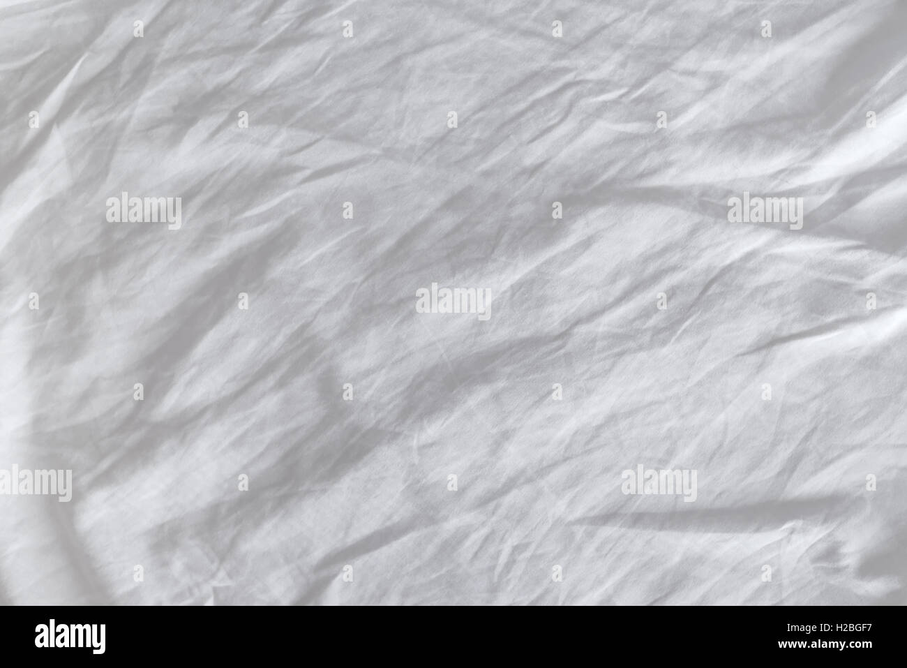 Crumpled white cotton sheets texture, top view of wrinkles on an untidy bed. Stock Photo
