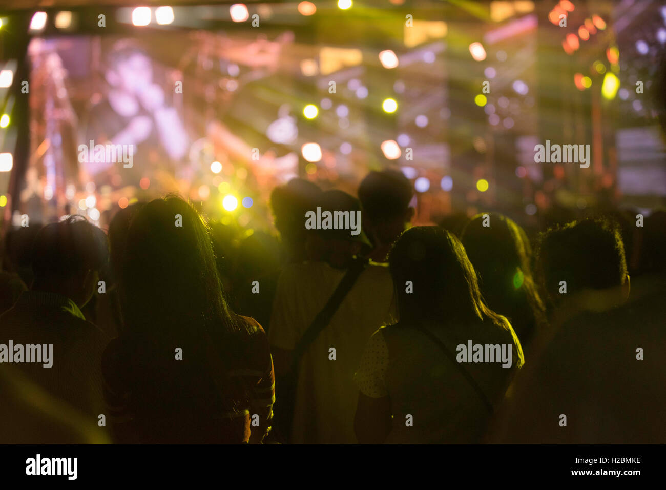 Audience at a music festival and lights streaming down from above the stage. Soft focus, high ISO, grainy image. Stock Photo