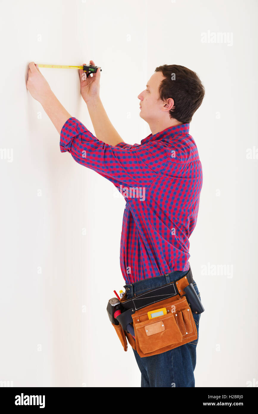 Young worker handyman with measuring tape near the wall in room Stock Photo