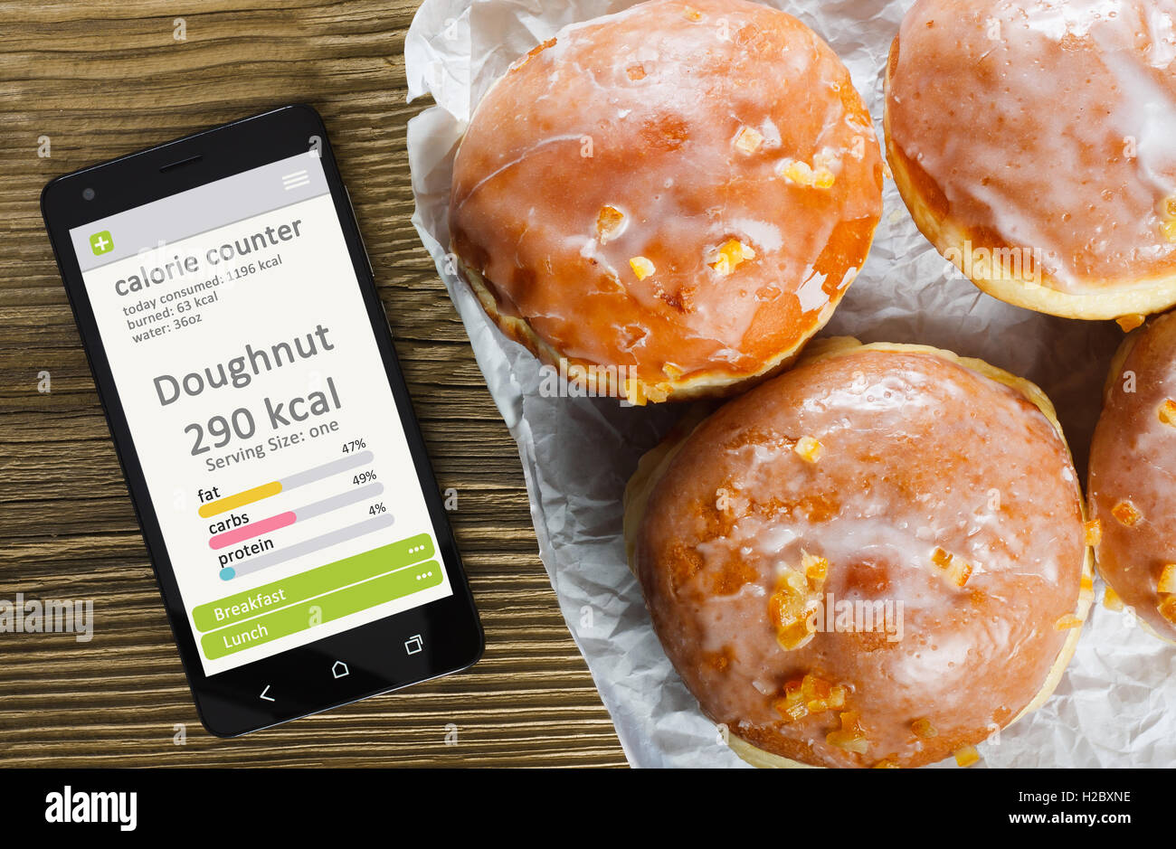 Calorie counter concept - mobile phone with calorie counter app on the screen and doughnuts. Wooden table as background Stock Photo