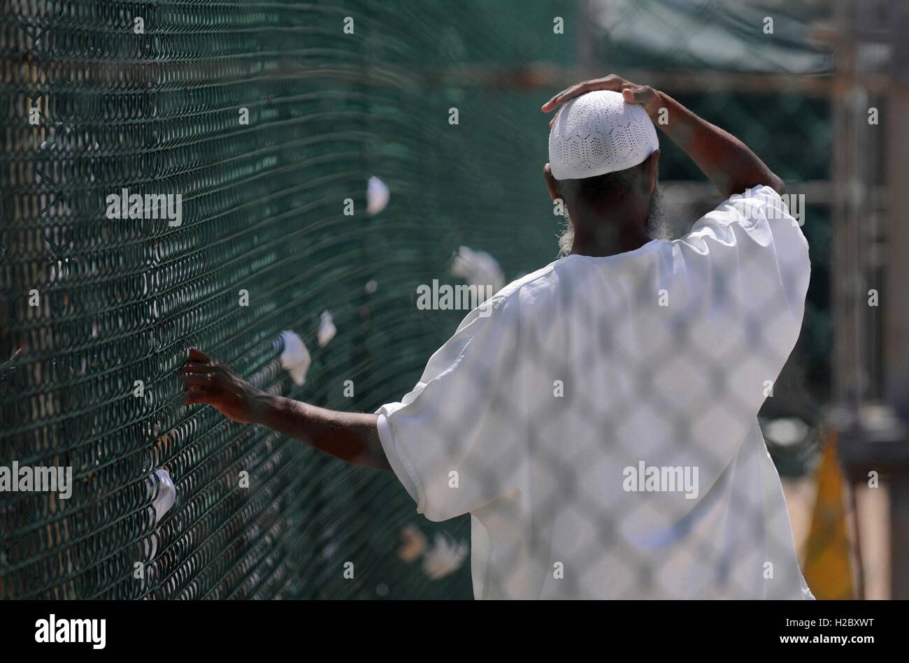 An inmate from the war on terror holds onto a chain link fence while standing in a recreation yard at Joint Task Guantanamo Camp IV June 8, 2010 in Guantanamo Bay, Cuba. Stock Photo