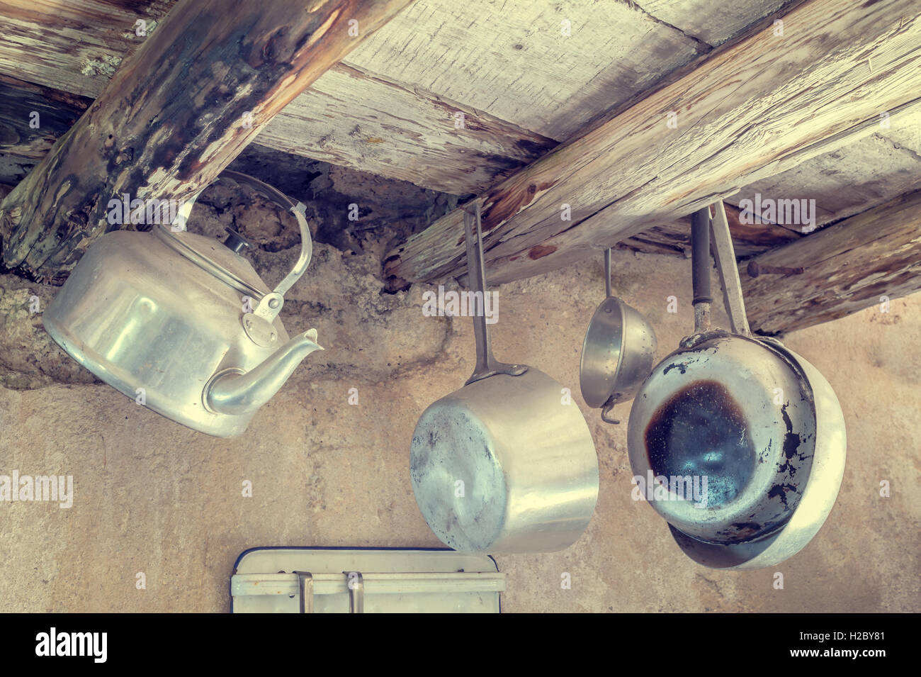 Old kitchen utensils in aluminum. Hanging from old wooden beams, pans, strainer, kettle.  Photo in styles vintage Stock Photo