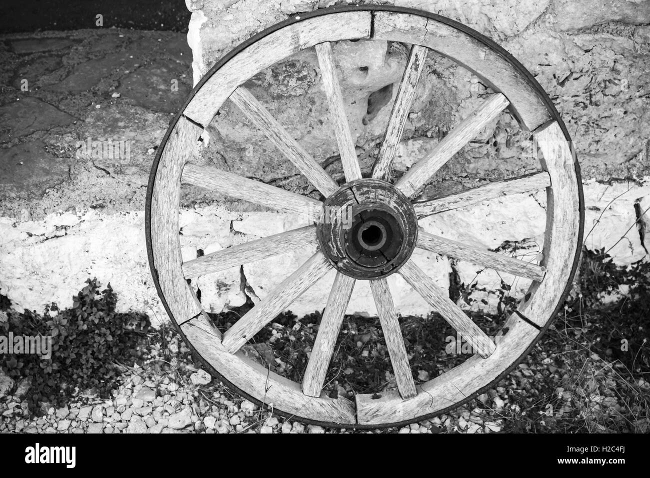 Old wooden wheel stands near stone rural wall, black and white retro style photo Stock Photo