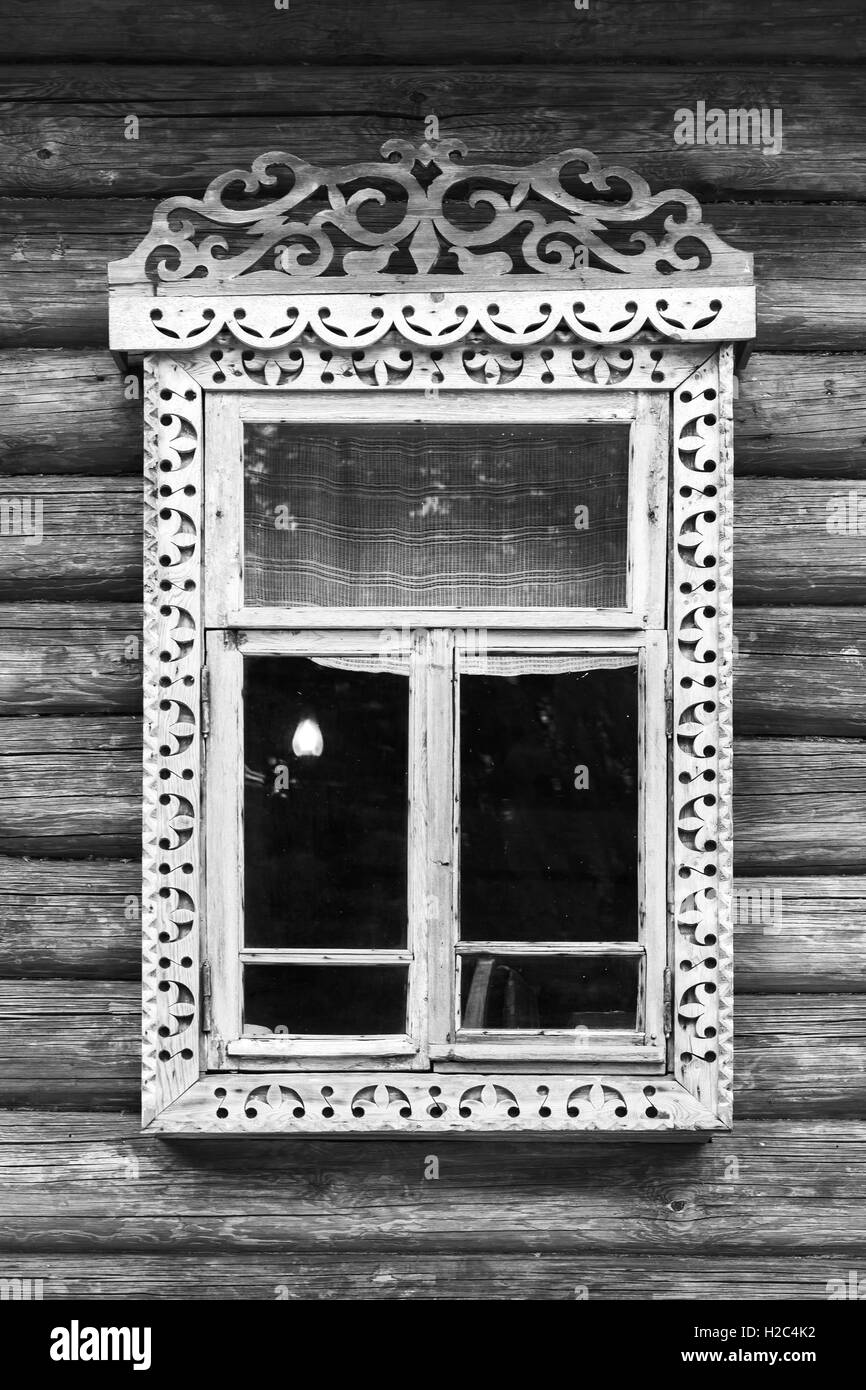 Traditional rural Russian architecture details. Window with carved wooden frame in wall made of rough logs, black and white retr Stock Photo