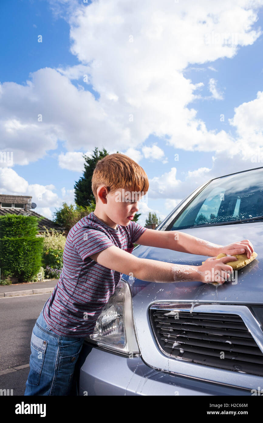 A young boy washing a metallic silver Vauxhall Meriva car outside on a sunny day Stock Photo