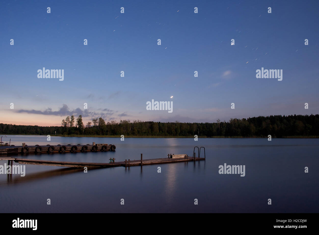 Nightscape (landscape) with sunrise, stars that are reflected in the water surface (star trails are visible) Stock Photo