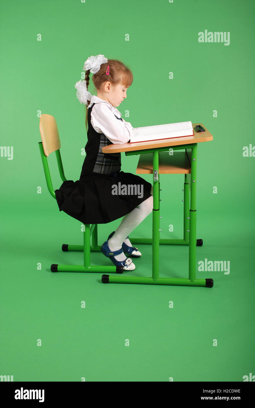 Girl in a school uniform sitting at a desk and reading a book isolated ...