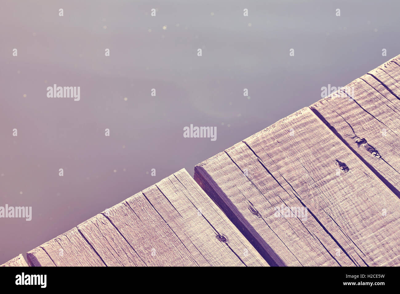 Vintage toned close up photo of an old wooden pier by a lake, background with space for text. Stock Photo