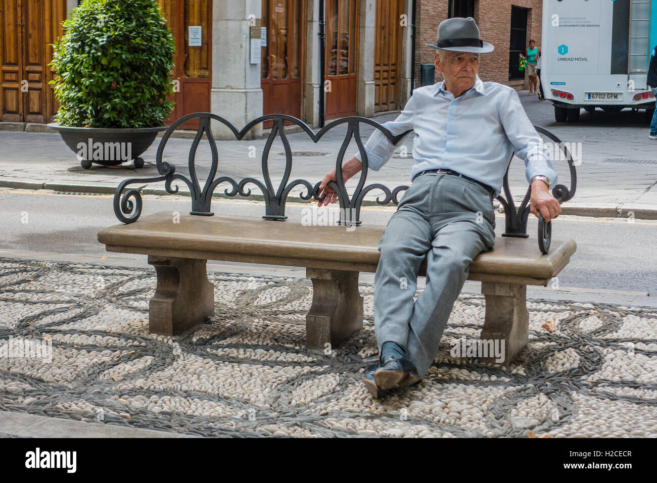 An older Spanish male sits on a park bench, relaxing, in Granada, Spain