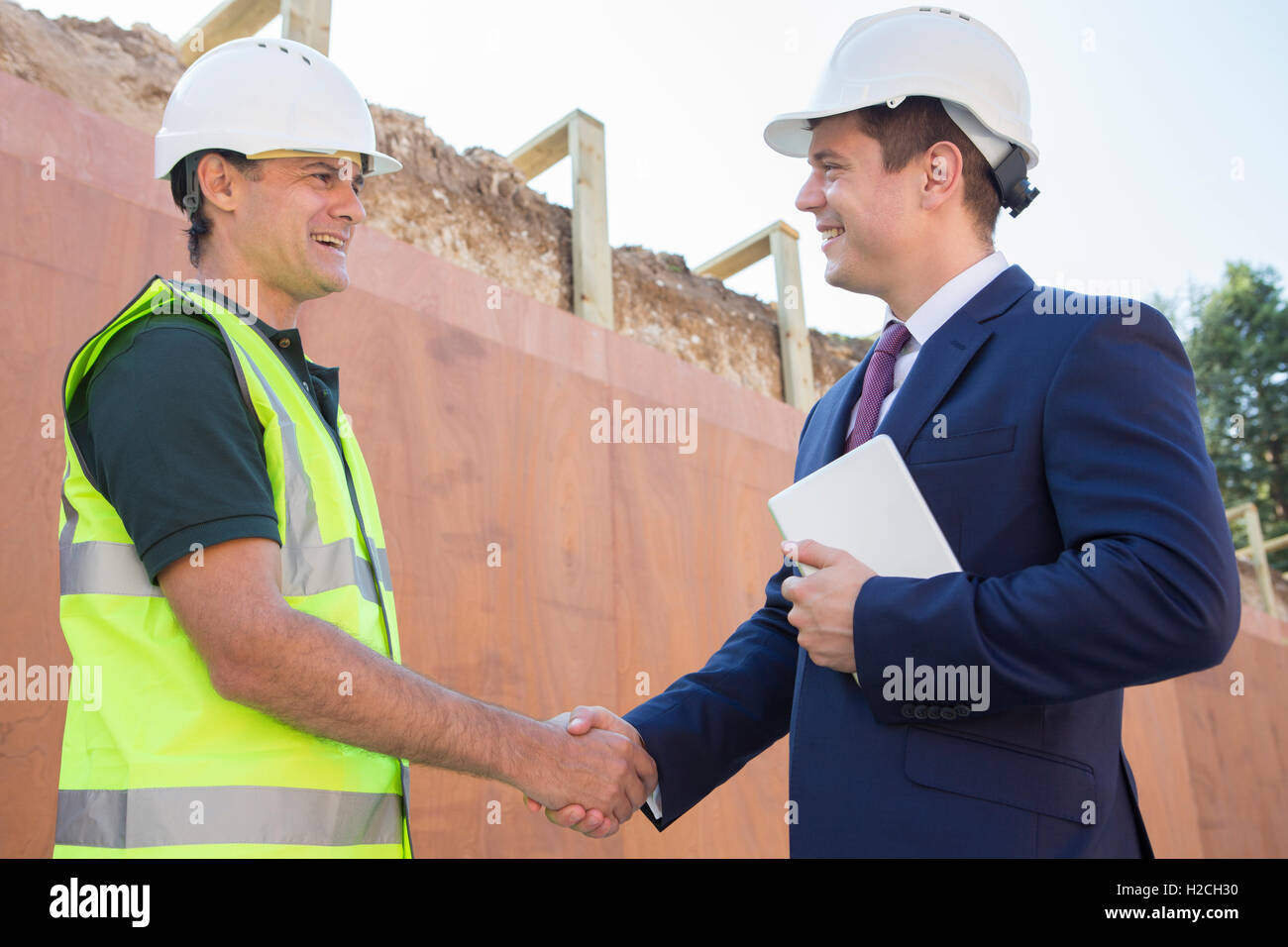 Businessman Shaking Hands With Builder On Construction Site Stock Photo