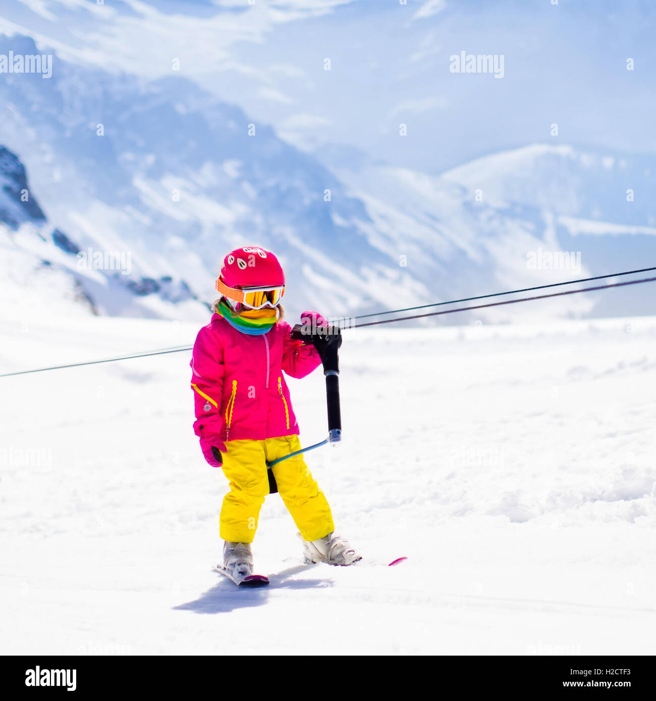 Child on a button ski lift going uphill in the mountains on a sunny