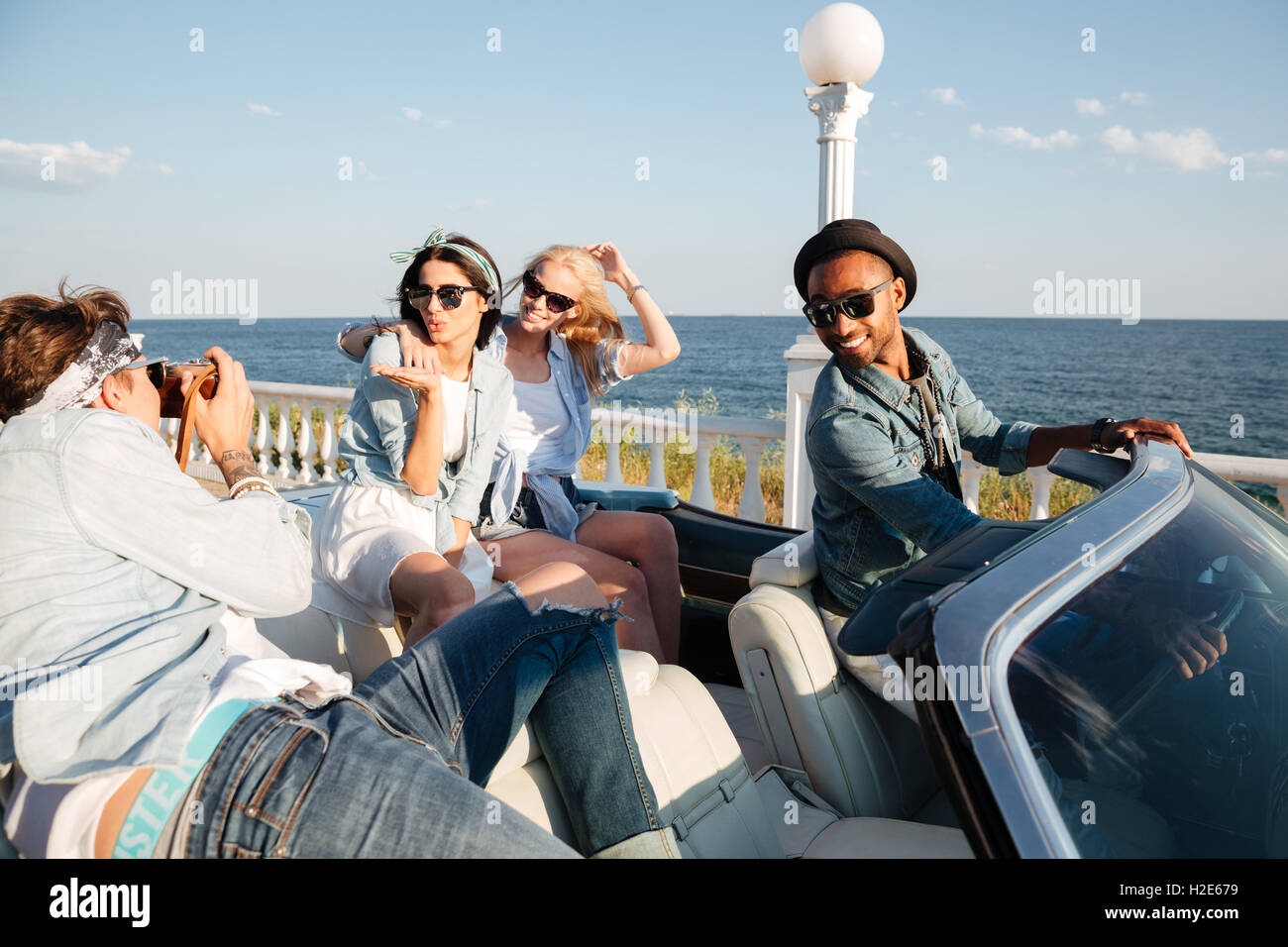 Multiethnic group of happy young people taking photos in cabriolet in summer Stock Photo