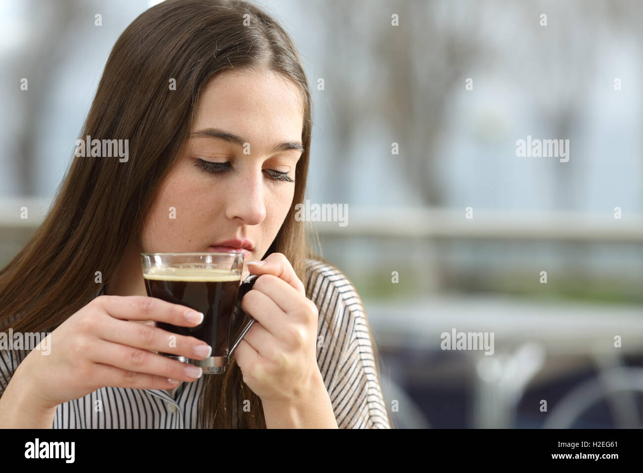 Portrait of a sad woman holding a coffee cup thinking and looking down sitting in a restaurant in a rainy day Stock Photo