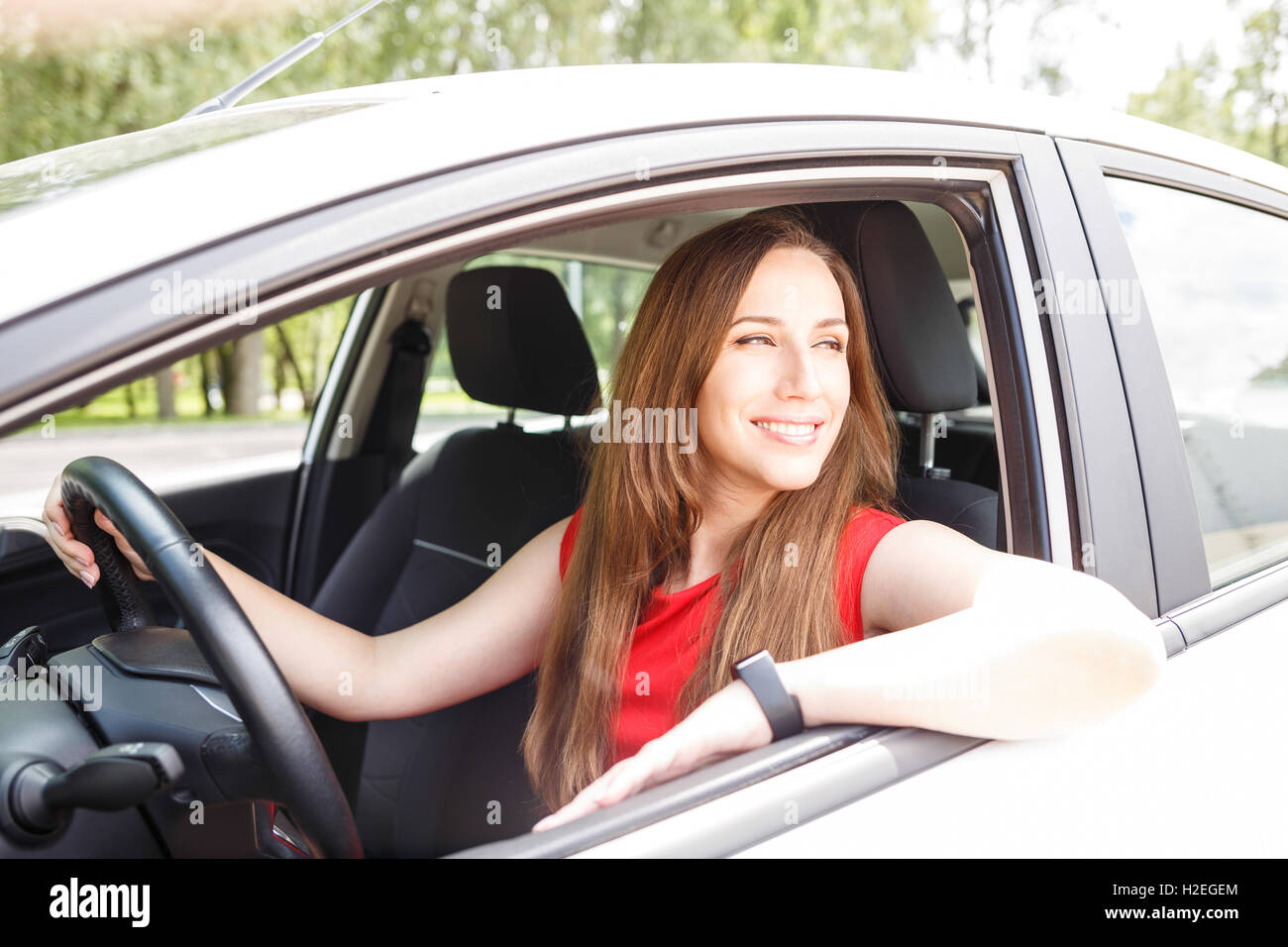 Young confident woman in red dress sitting in the car and holding wheel Stock Photo