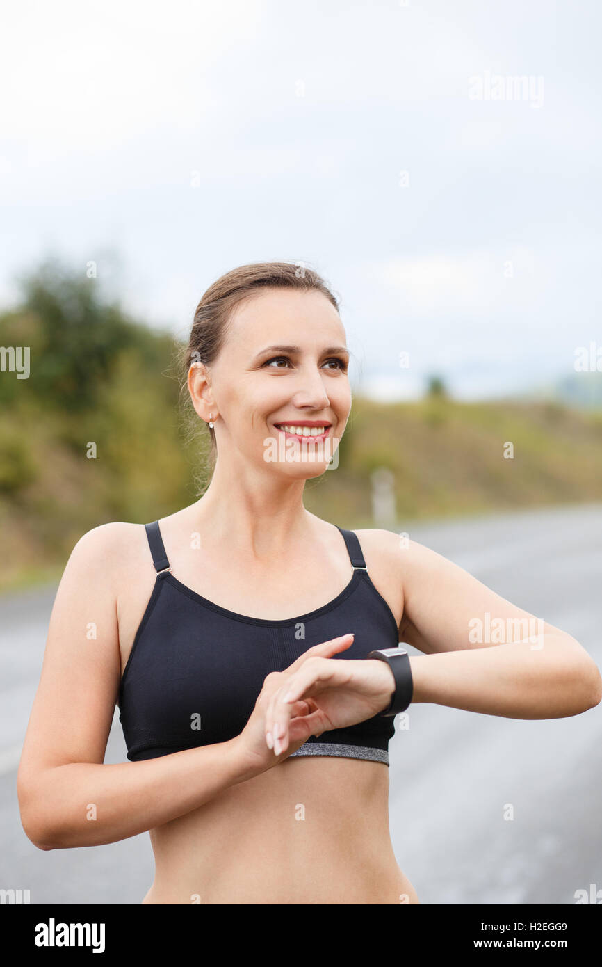 Young smiling fitness woman using her smart watch for heartrate after jogging. Healthy caucasian girl with fitness tracker watch Stock Photo