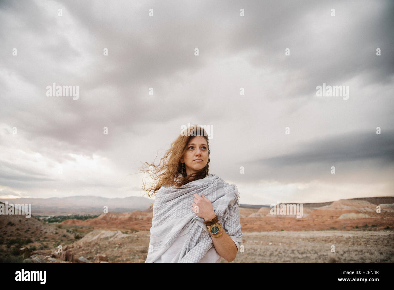 A woman with windblown hair wrapped in a shawl in a desert landscape Stock Photo