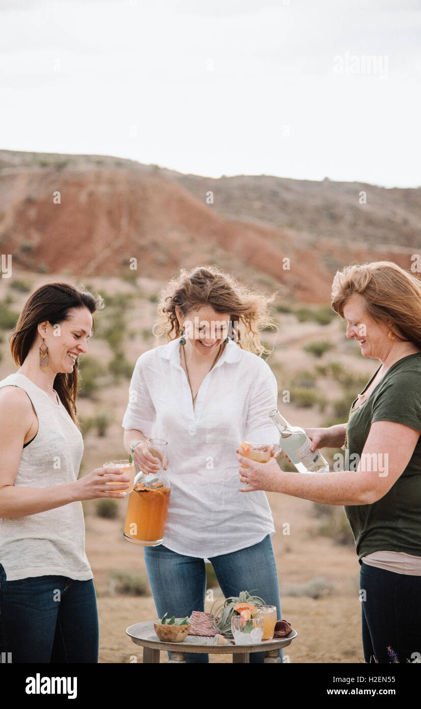Three women standing in a desert landscape having a drink. Stock Photo