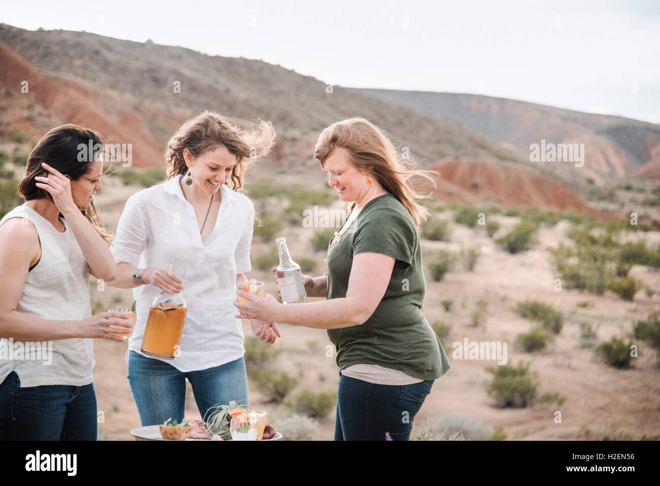 Three women standing in a desert landscape having a drink. Stock Photo