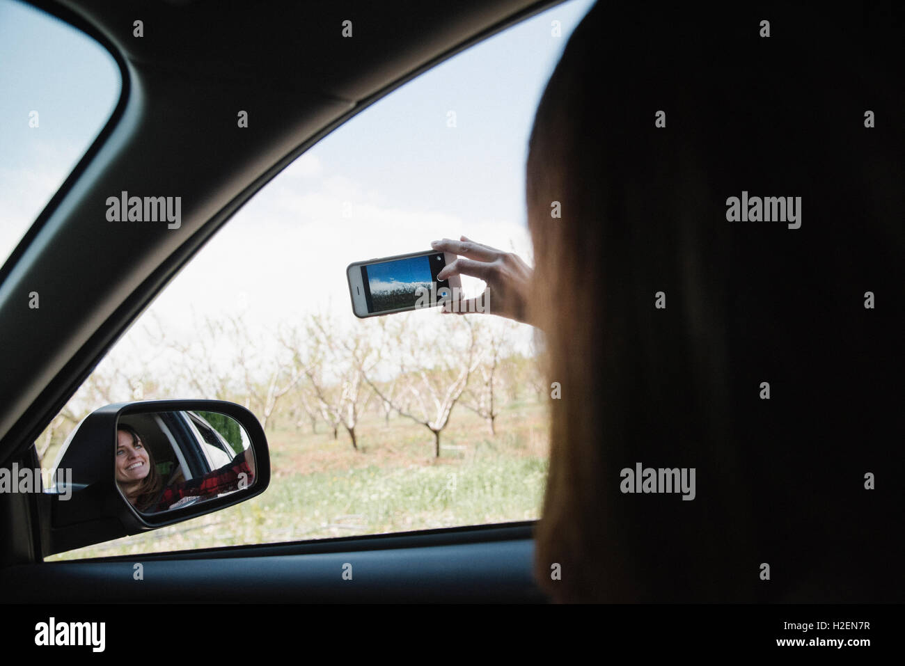 Woman in a car on  a road trip, taking a picture out of the car window with a phone. Stock Photo