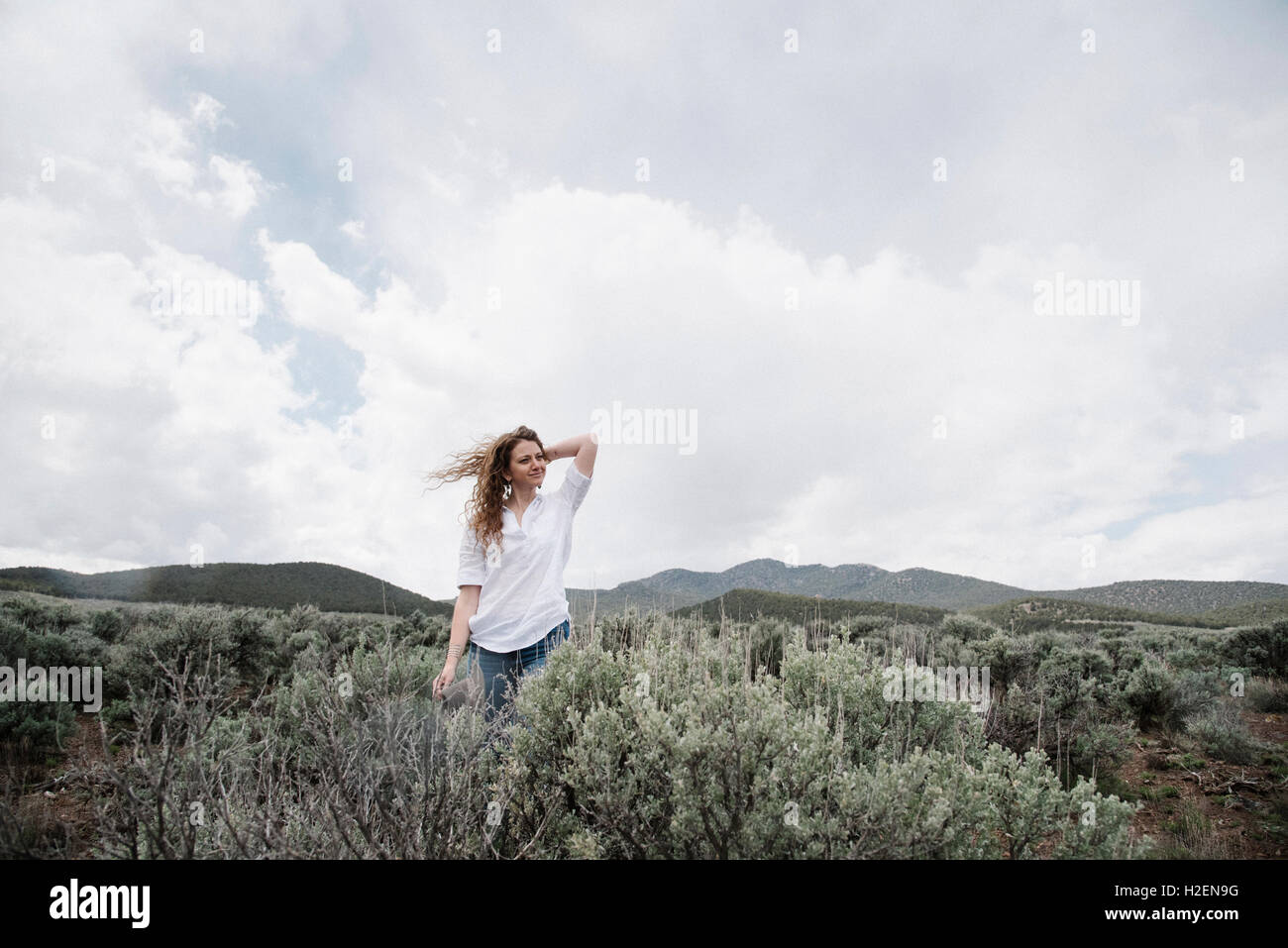 A woman standing in an open landscape with a view of mountains woodland and scrub land. Stock Photo