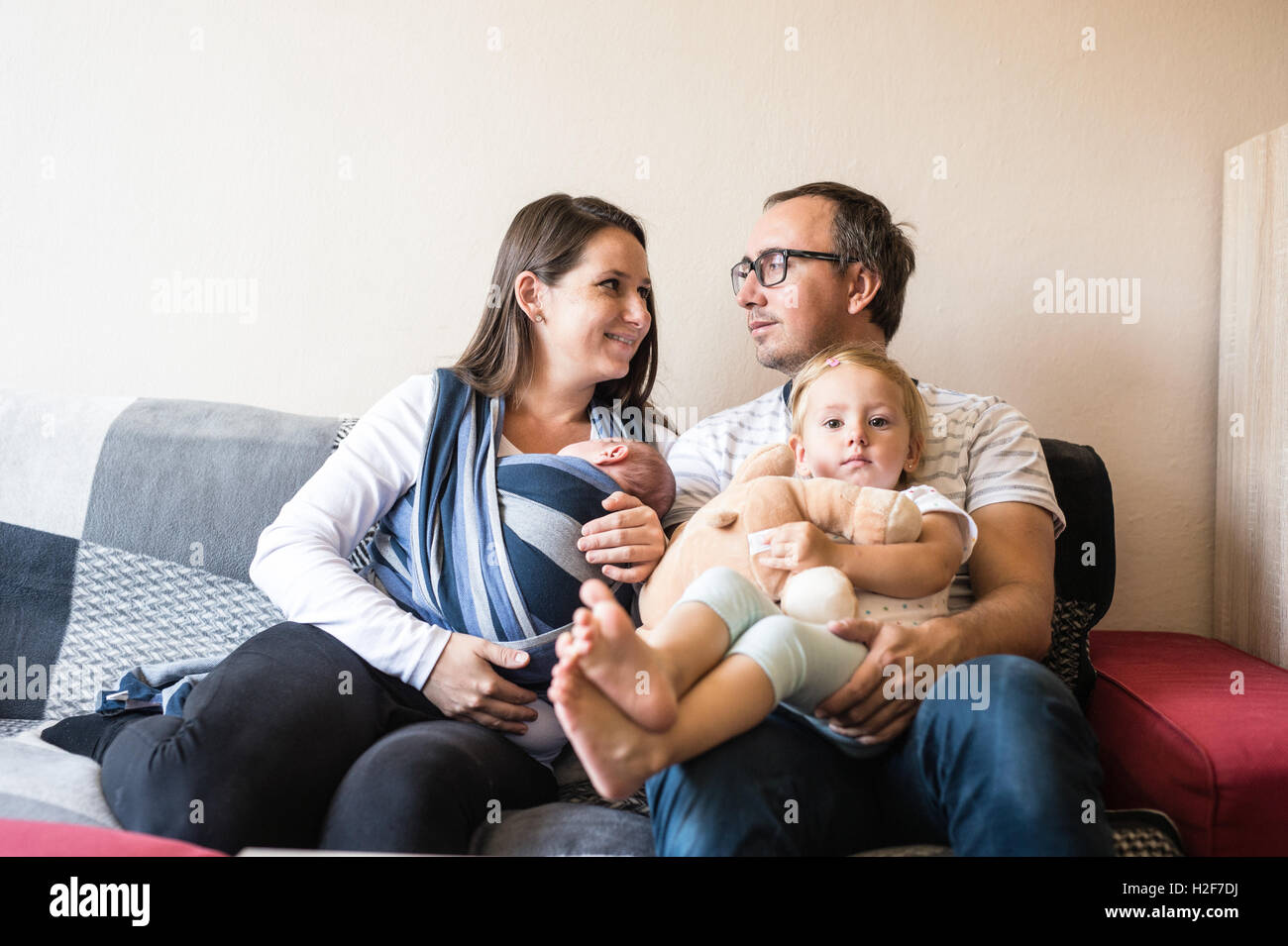 Young parents with children sittin on sofa, baby sling Stock Photo