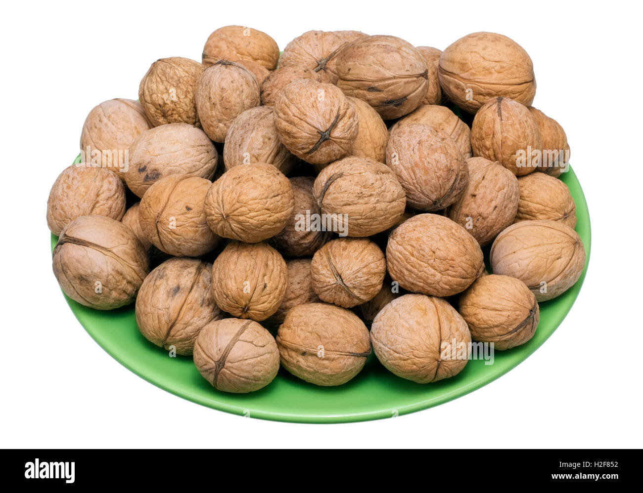 The real crude walnuts heap lie on a green ceramic plate. Isolated on white Stock Photo