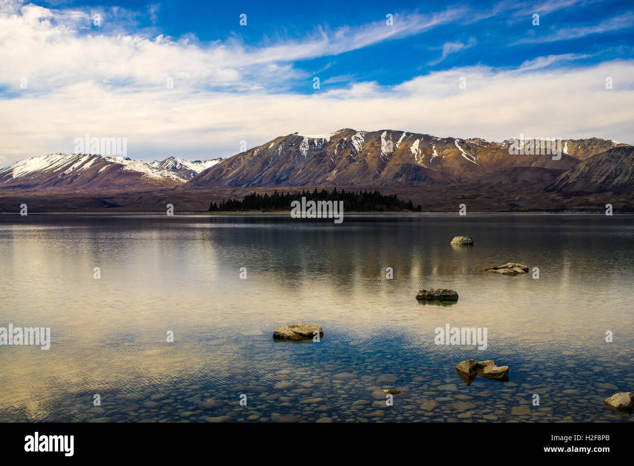 An island in a crystal clear alpine lake with snow capped mountains in ...
