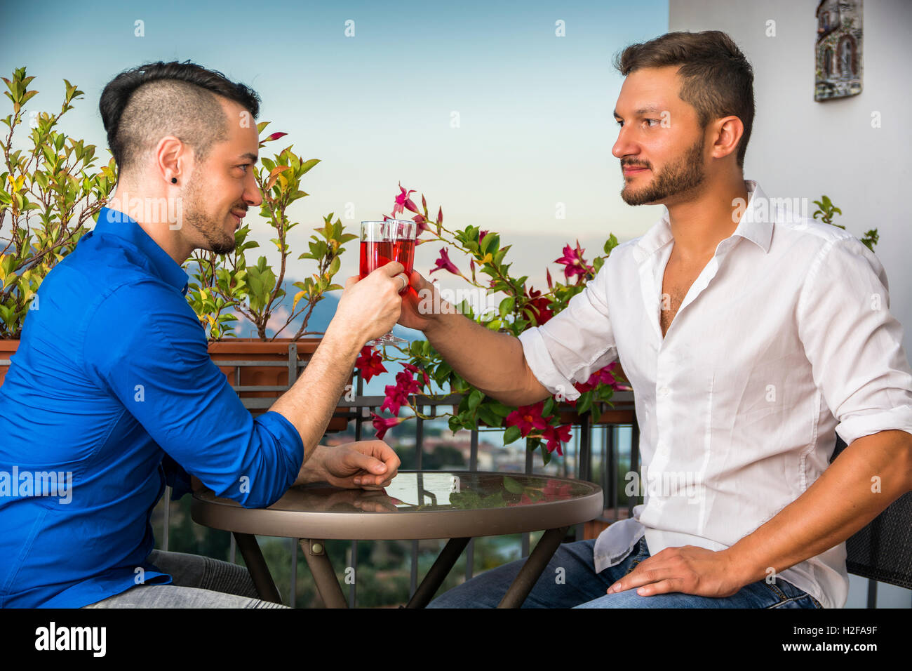 SIde view of two stylish handsome men sitting at the table with glasses of wine while looking face to face Stock Photo