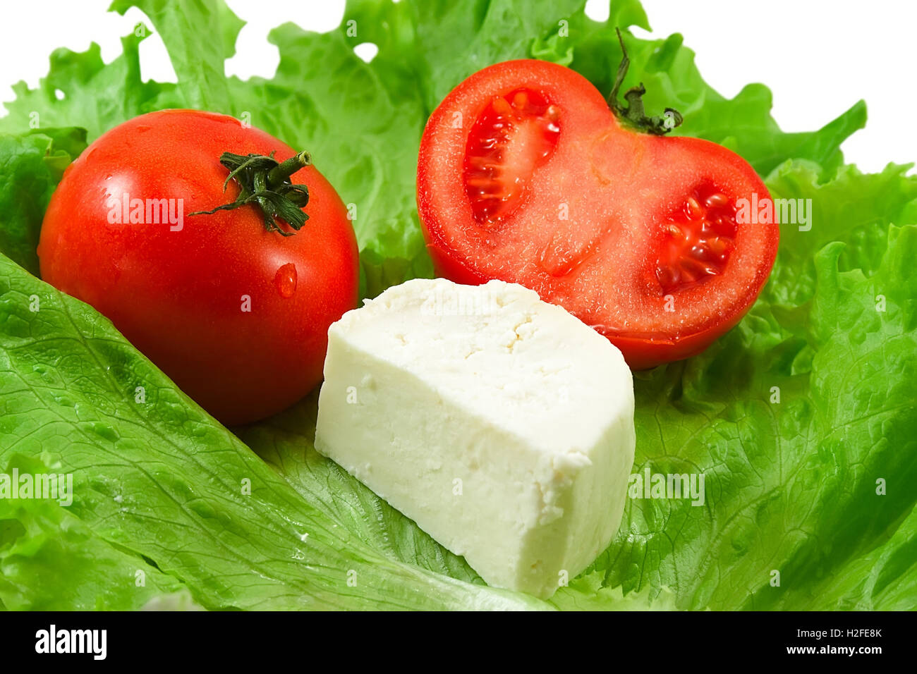 Red tomatos with waterdrops and cheese on  salad leaves closeup isolated on white background. Stock Photo