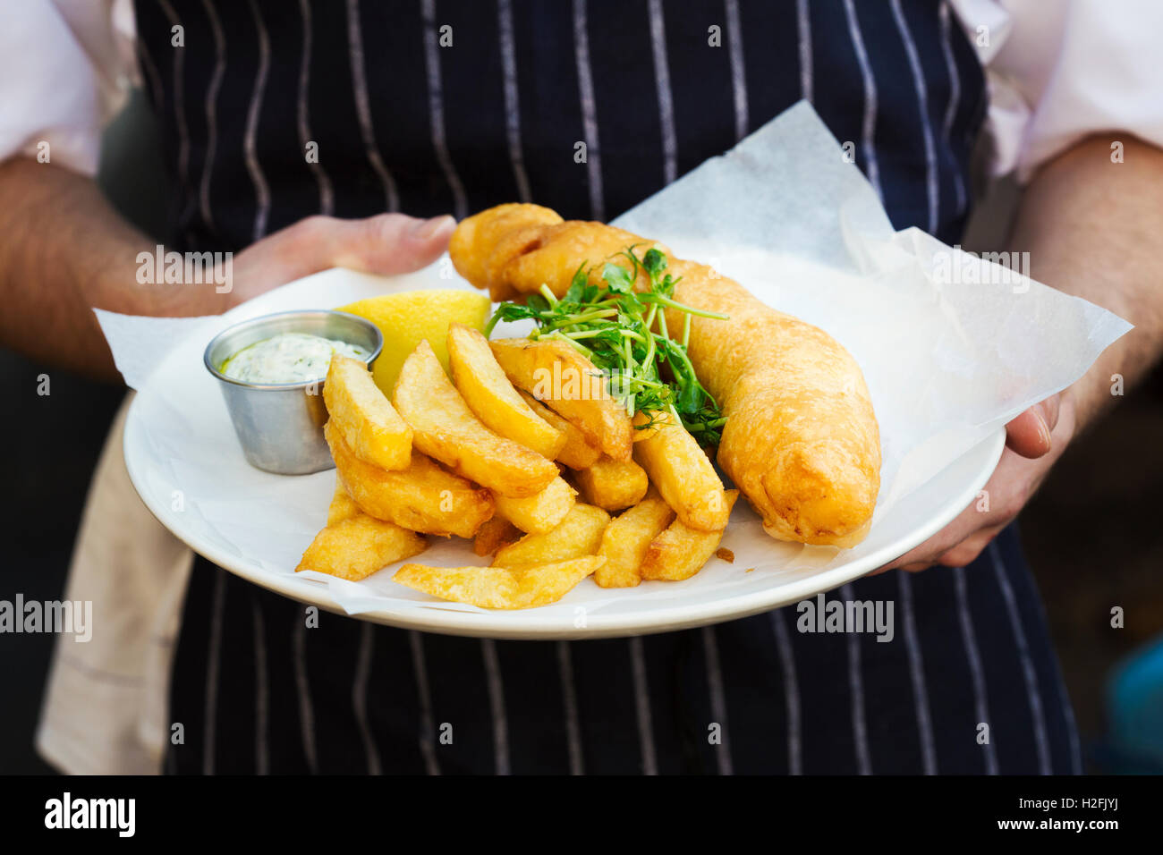A cooked meal, a dish of fish and chips with garnish and tartare sauce. Stock Photo