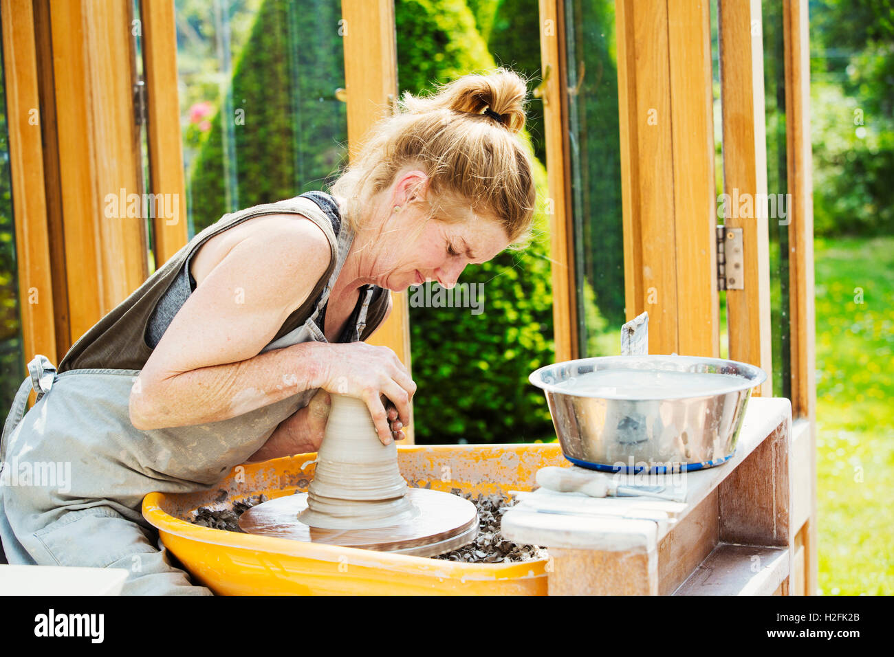 A woman potter working clay on  a potter's wheel in her workshop. Stock Photo