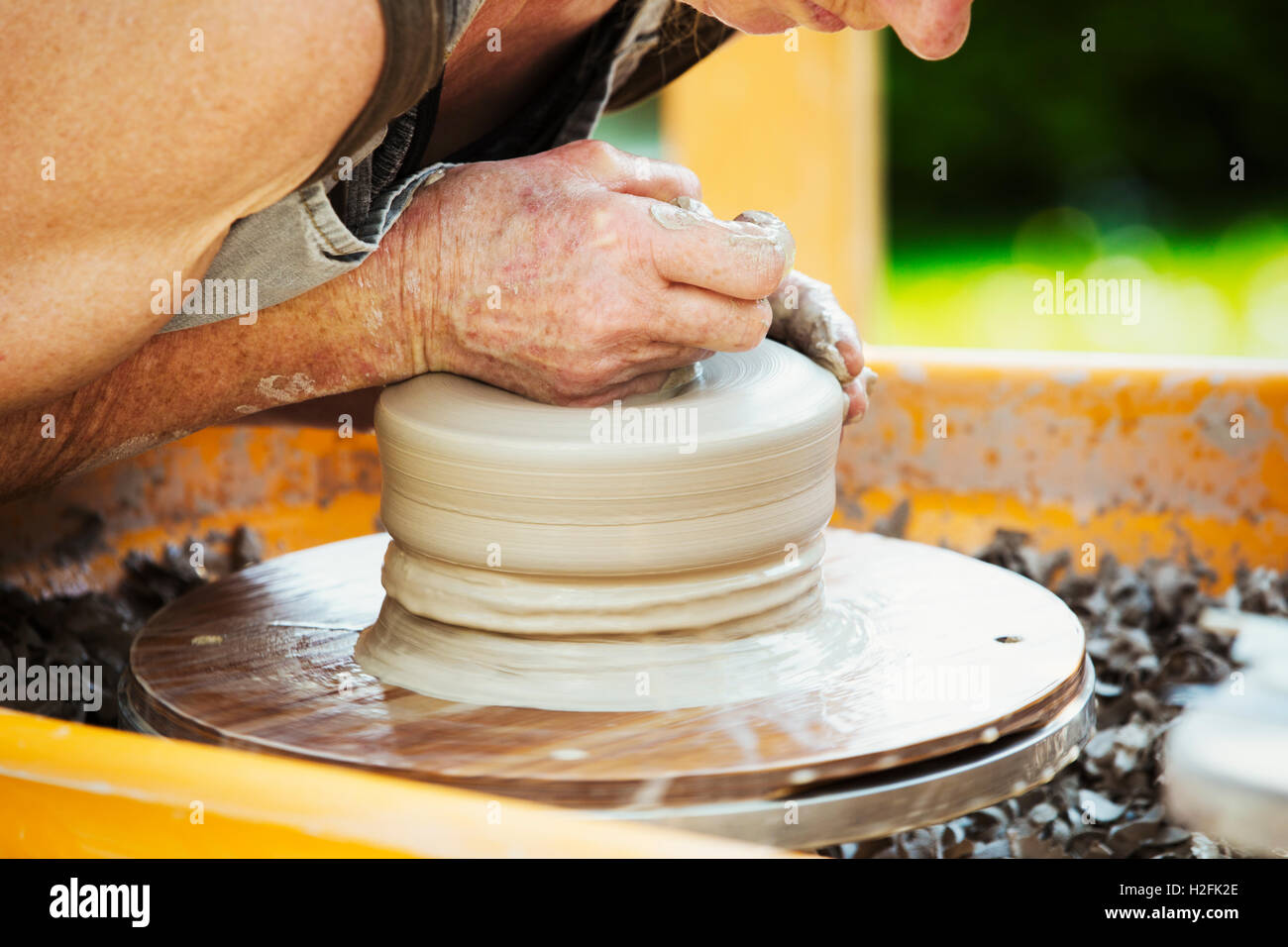 A woman potter working clay on  a potter's wheel in her workshop. Stock Photo