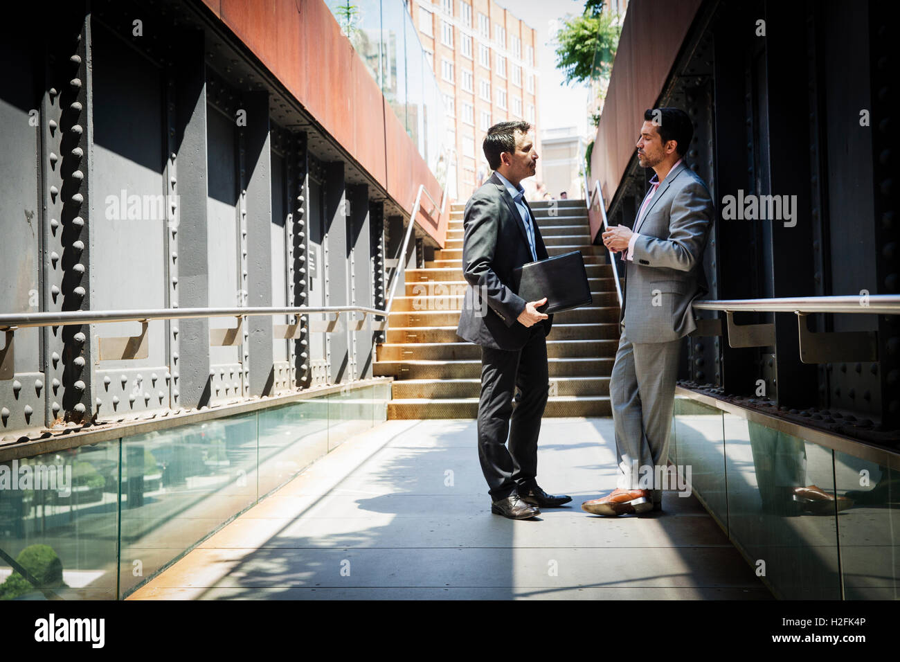 Two businessmen wearing grey suits standing outdoors, talking to each ...