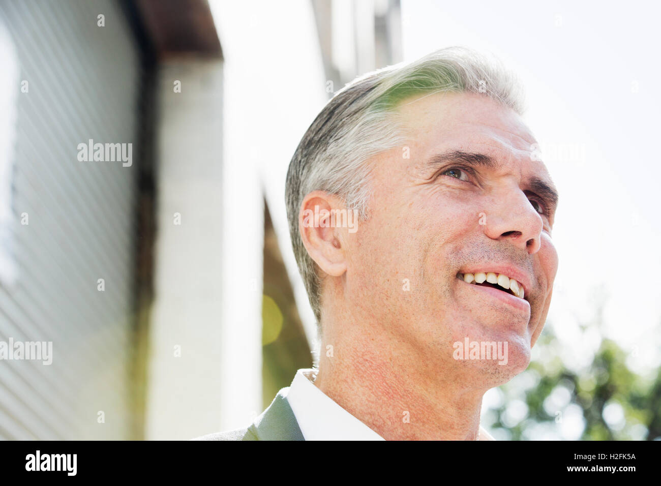 A man with grey hair standing on a street looking up and smiling confidently, looking up view from below. Stock Photo