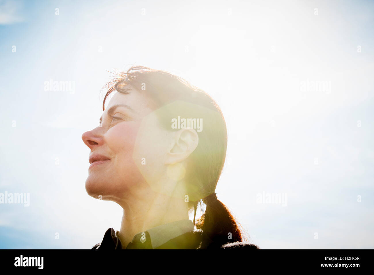 A woman, low angle view, side profile, looking upwards. Lens flare. Stock Photo