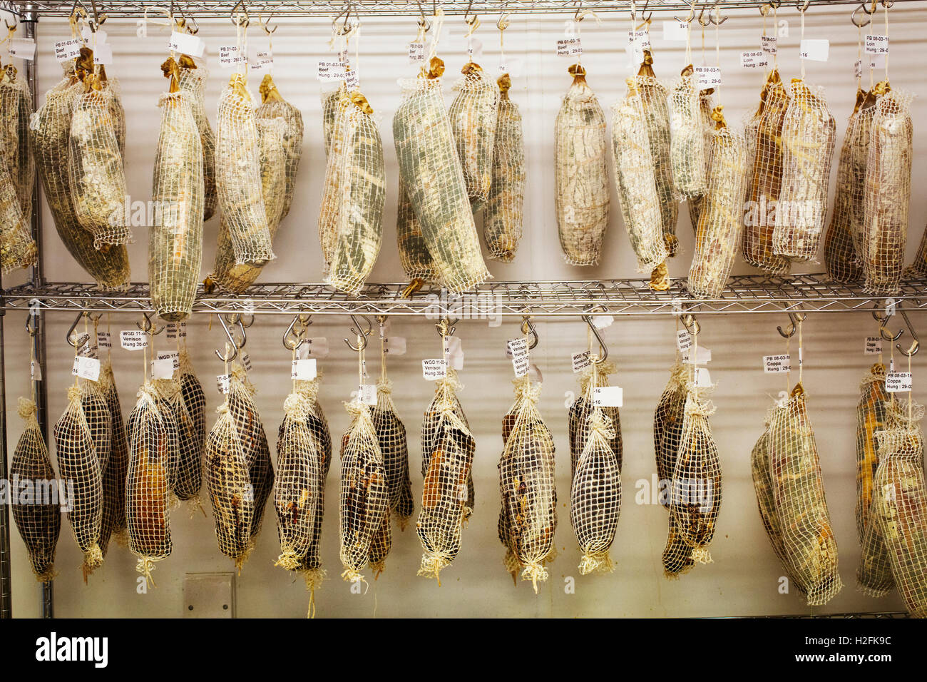 Pieces of air dried beef, venison  and Coppa in nets, hanging from hooks in a charcuterie. Stock Photo