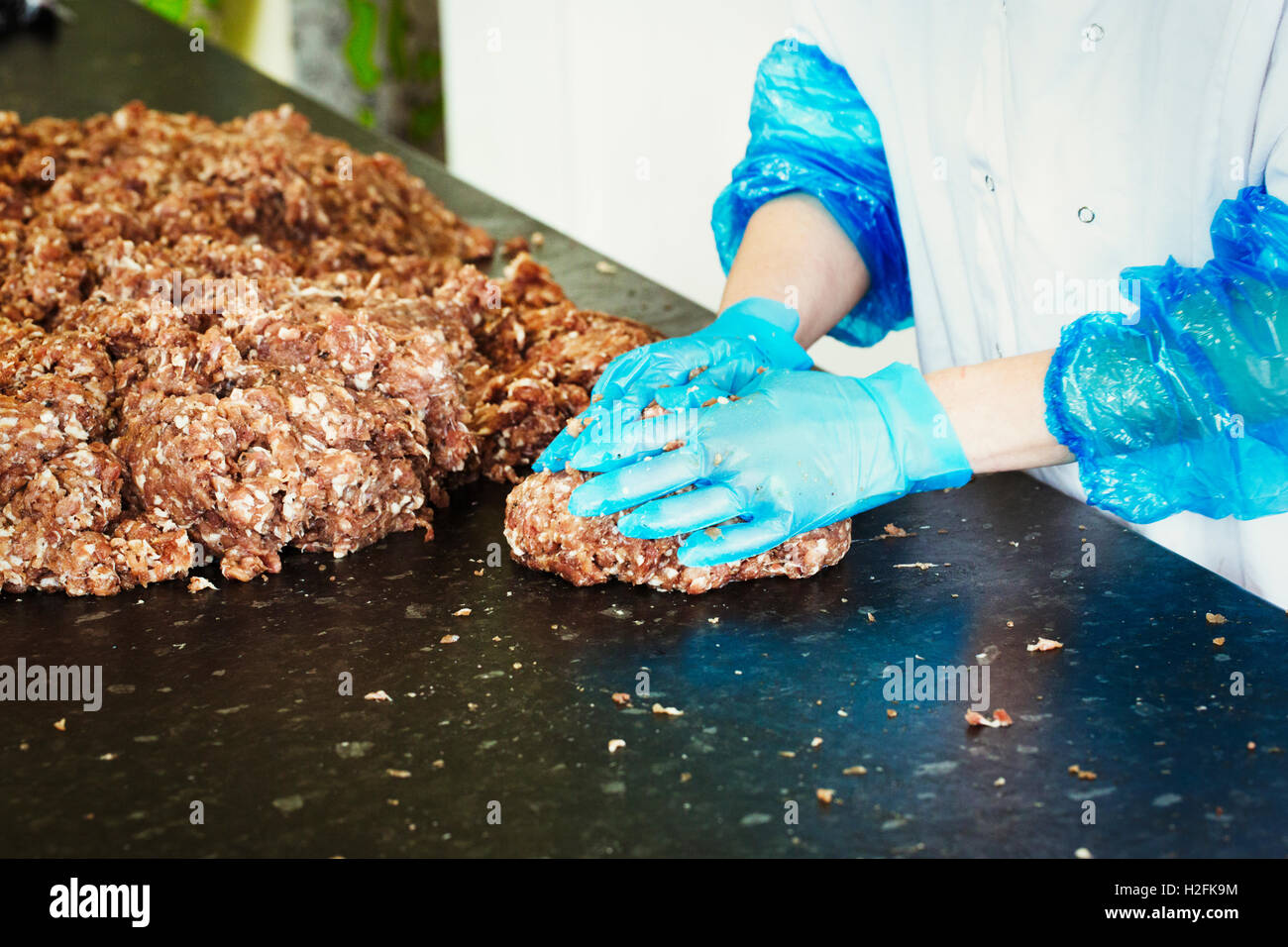 Woman working in a butchery, wearing protective clothes and gloves, shaping minced meat into patties. Stock Photo