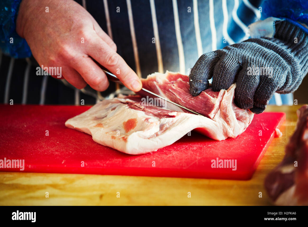 https://c8.alamy.com/comp/H2FKA6/butcher-wearing-a-striped-blue-apron-and-protective-glove-cutting-H2FKA6.jpg