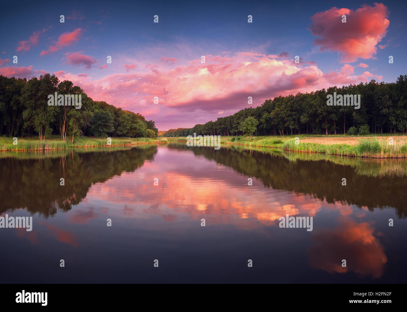 Beautiful panoramic landscape with colorful cloudy sky, sun, lake and trees in the evening. Summer sunset at the river Stock Photo