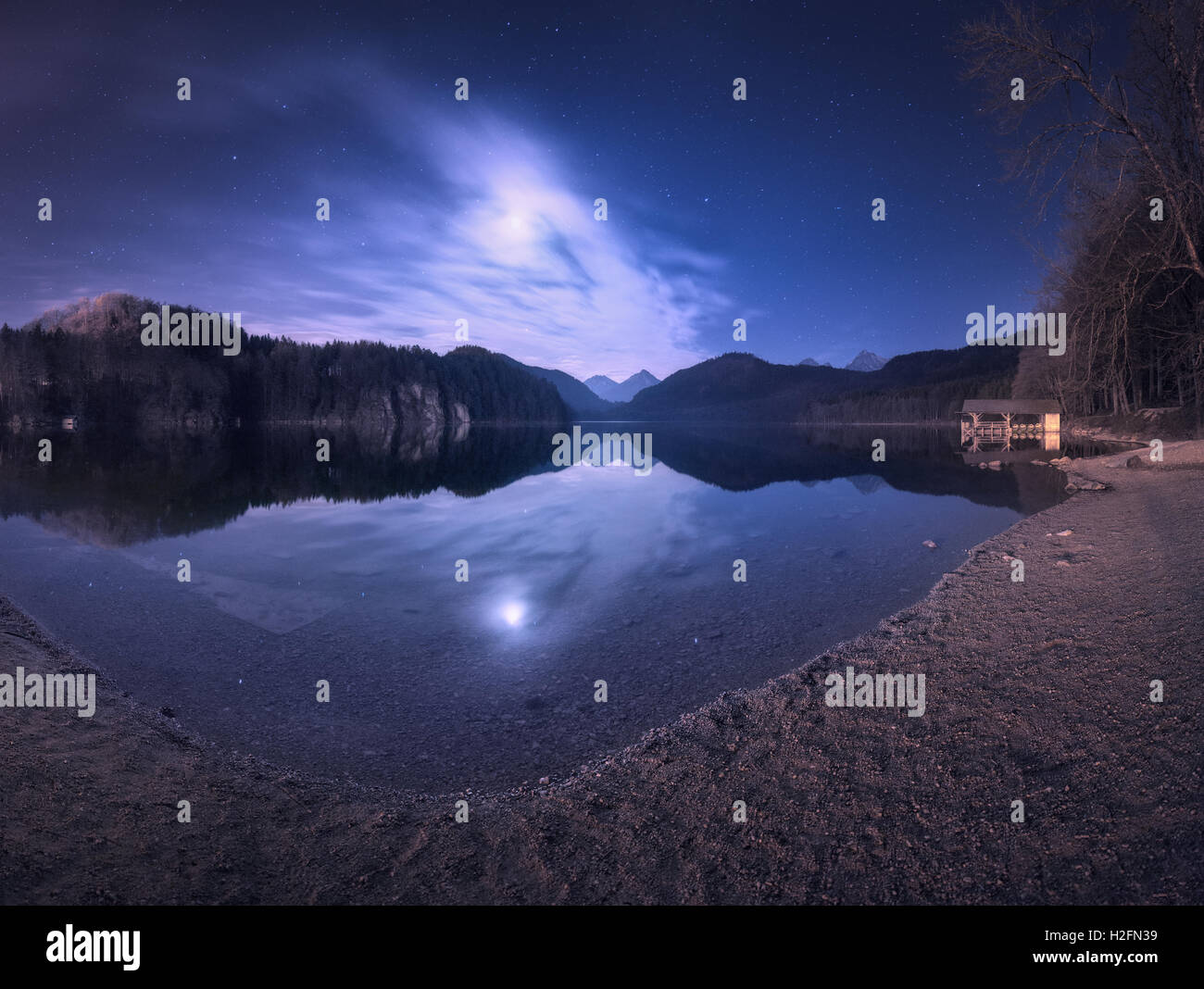 Colorful night landscape with lake, mountains, forest, stars, full moon, purple sky and clouds reflected in water. Spring night Stock Photo