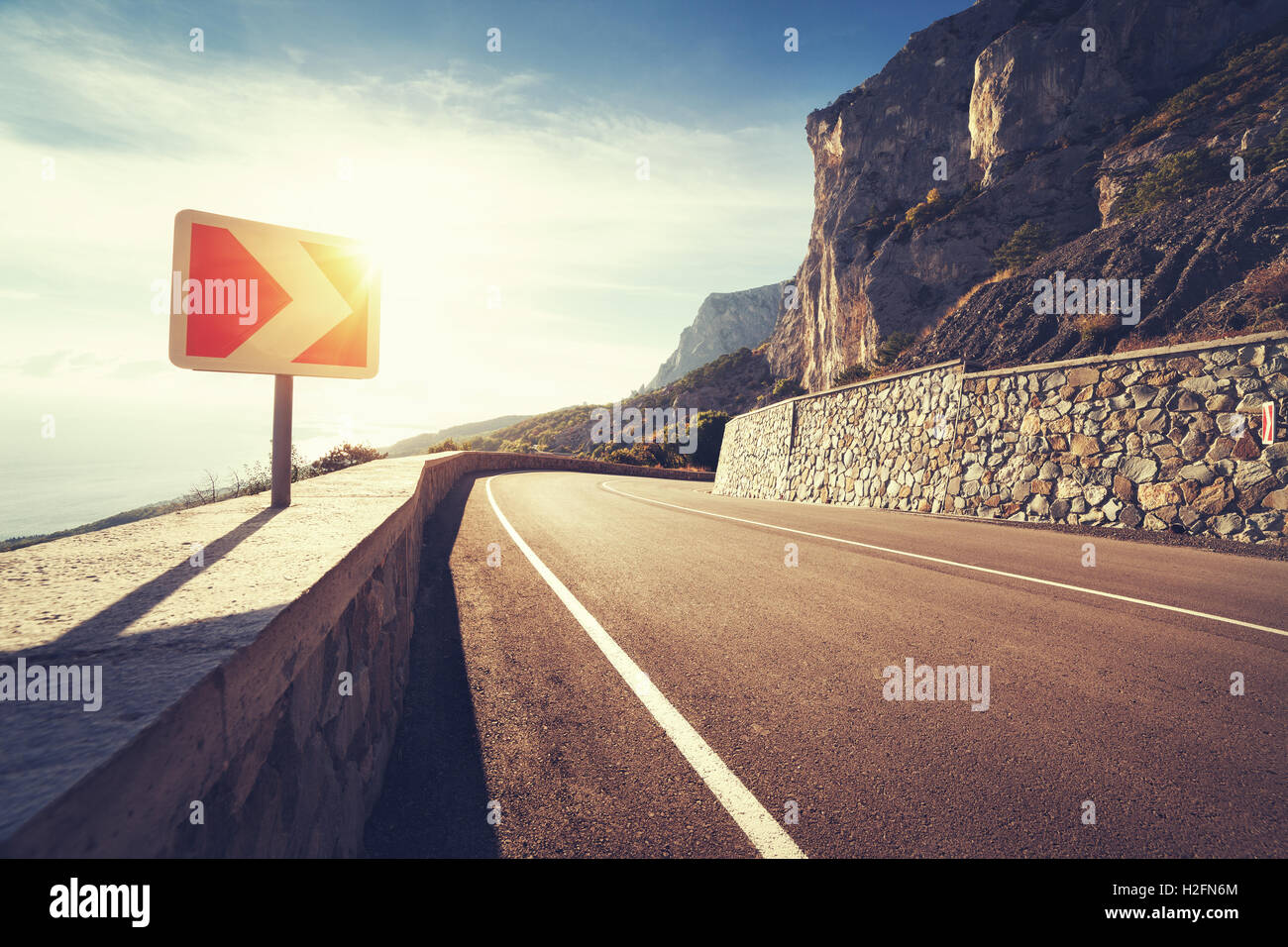 Asphalt road and road sign in mountains at sunrise with vintage toning. Beautiful landscape with mountain highway, road sign, bl Stock Photo