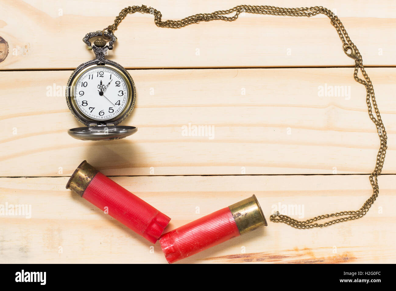 Red shotgun shell, antique clock placed on a wooden floor. Stock Photo