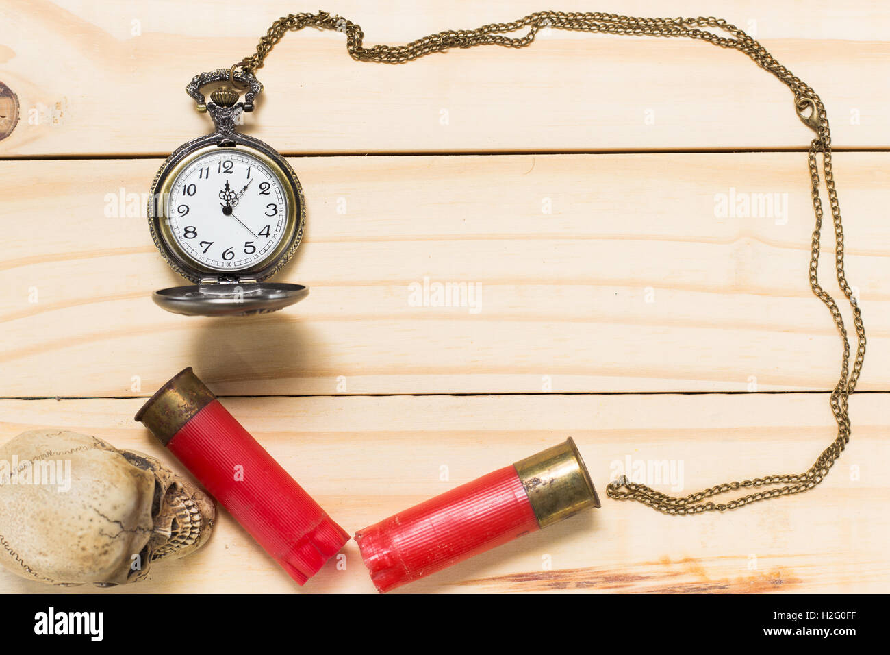 Top view human skulls, red shotgun shell, antique clock placed on a wooden floor. Stock Photo