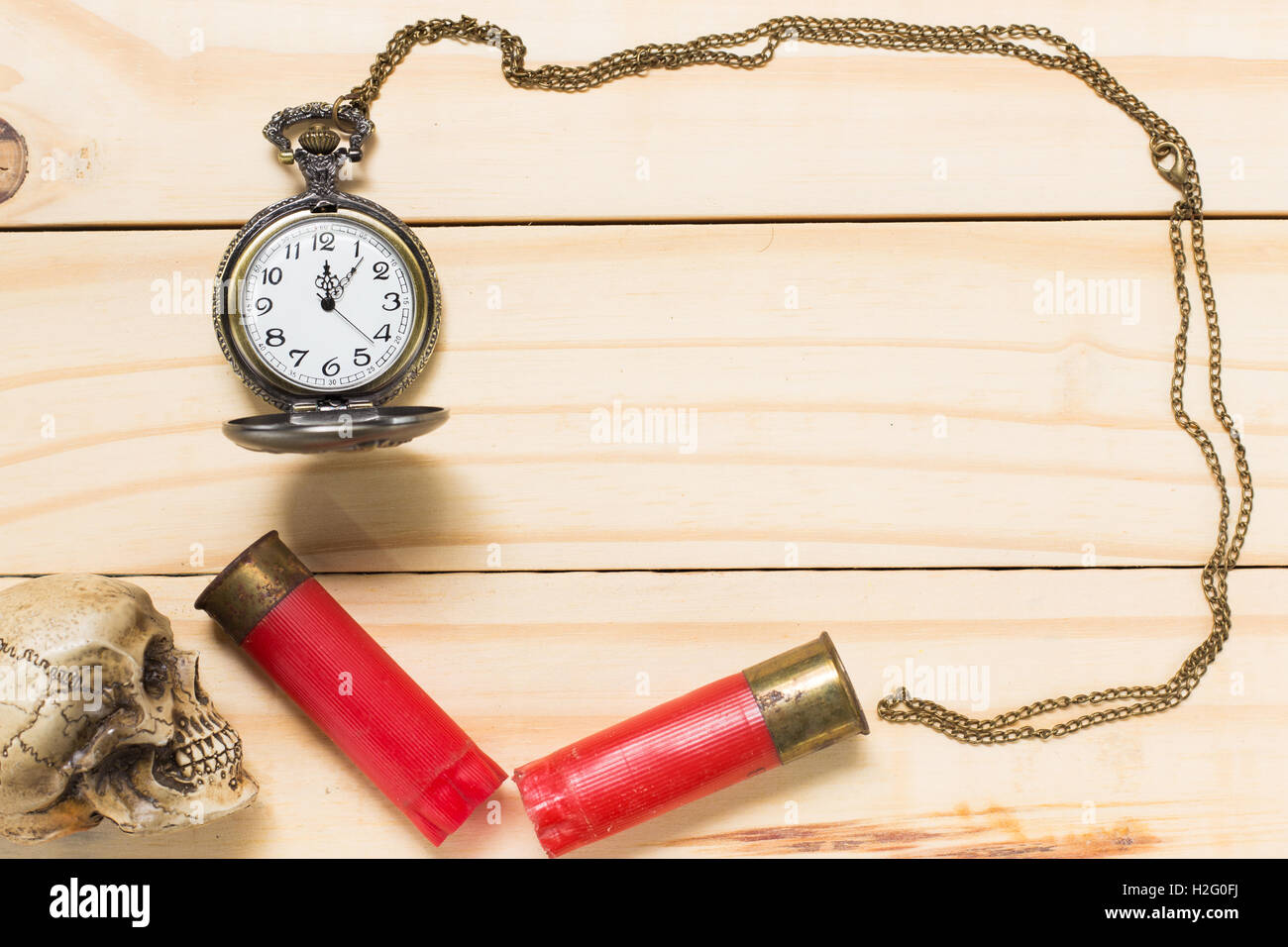 Top view human skulls, red shotgun shell, antique clock placed on a wooden floor. Stock Photo